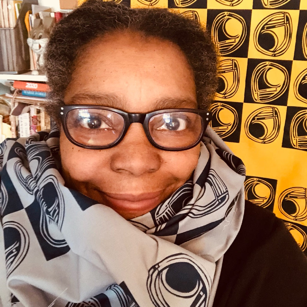 image of pantera saint-montaigne, owner of brooklyn mojo. Pantera is a Black woman with black glasses and is wearing a hand printed scarf of her design.