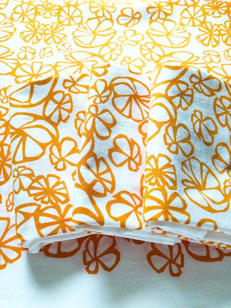 an image of an open orange kitchen towel with 3 folded towels on top. Each towel is decorated with the same abstract floral design.